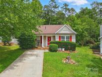 Charming one-story home featuring red accents, manicured lawn and mature trees at 1006 Washburn Ct, Monroe, NC 28110