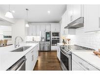 Modern white kitchen features stainless steel appliances, subway tile backsplash, and dark wood flooring at 10901 Greenvale Dr, Harrisburg, NC 28075