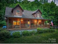 Charming log cabin with inviting covered porch and an American flag, nestled in a lush green setting at 95 Odell Ct, Taylorsville, NC 28681