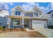 Two-story home with gray siding, stone accents, two-car garage, covered porch and beautifully landscaped front yard at 128 Longwood Rd # 51, Mooresville, NC 28115