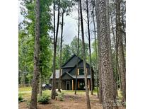 Modern farmhouse with dark siding nestled in trees, featuring a garage and natural wood porch columns at 3020 Quiet Ln, Iron Station, NC 28080