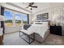Bright main bedroom featuring three windows, a tray ceiling and a patterned accent wall at 3118 Stelfox St, Charlotte, NC 28262