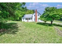 Charming two-story home featuring a brick chimney, metal roof, and lush green lawn with mature trees at 5604 Nc 152 E Hwy, Rockwell, NC 28138