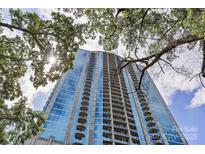 Striking building exterior showcases a modern design with glass windows and private balconies, framed by leafy trees at 210 N Church St # 2910, Charlotte, NC 28202