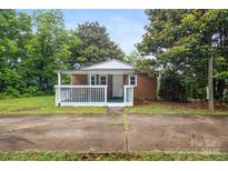 Charming brick home featuring a cozy, covered front porch with white railings, surrounded by lush greenery at 653 Turner St, Mooresville, NC 28115