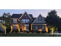 Beautiful two-story home with stone facade and professional landscaping, illuminated by landscape lighting at dusk at 2414 Madeira Cir, Waxhaw, NC 28173