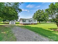 Charming single-story home with green shutters, a lush lawn, storage shed, and gravel driveway at 338 Hickory Grove Rd, Harmony, NC 28634