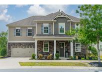 Inviting two-story home featuring stone accents, gray siding, a well-manicured lawn, and a charming front porch at 515 Lizzie Ln, Fort Mill, SC 29708
