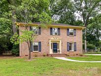 Charming brick two-story home with blue shutters, mature trees, and manicured front yard at 1049 Regency Dr, Charlotte, NC 28211