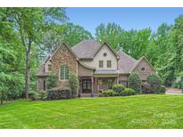 Beautiful brick and stone two-story home with mature trees and lush landscaping on a well-manicured lawn at 1056 James Madison Dr, Matthews, NC 28104