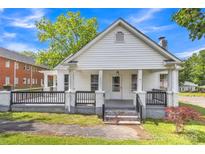 Charming home featuring a cozy front porch and black railing, complemented by green grass and blue skies at 111 E Church St, Stanley, NC 28164