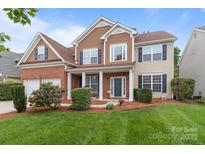 Inviting two-story home featuring a manicured lawn, brick accents, and a charming covered front porch at 1572 Edenton Nw St, Concord, NC 28027
