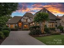 Elegant Tudor-style home showcasing stone accents and a meticulously landscaped front yard under a vibrant sunset sky at 18718 Peninsula Cove Ln, Cornelius, NC 28031