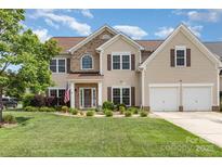 Two-story home featuring beige siding, an arched window, two-car garage, and an American flag displayed on the front porch at 9593 Indian Beech Nw Ave, Concord, NC 28027