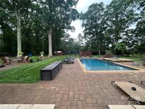 Backyard pool area with brick patio, lounge chairs, and mature trees providing shade at 12900 Westmoreland Rd, Huntersville, NC 28078