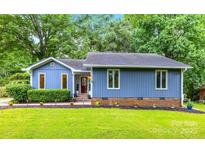 Charming single-story home with a manicured lawn, lush greenery, and a vibrant blue exterior at 13446 Idlefield Ln, Matthews, NC 28105