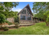 Stunning stone house with a striking window design, surrounded by lush greenery and landscaping at 1515 Heatherloch Dr, Gastonia, NC 28054