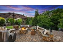 Stone patio featuring a fire pit and seating area with an umbrella table and wooded backdrop at 4430 Bravery Sw Pl, Concord, NC 28027
