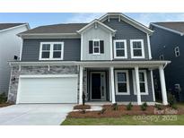 Charming two-story home featuring stone accents, gray siding, a white garage door, and a welcoming front porch at 1431 Hubert Graham Way, Tega Cay, SC 29708