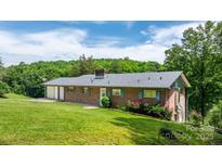 Brick home showcasing a well-manicured lawn, mature trees, and an attached garage, perfect for countryside living at 6256 Monford Dr, Conover, NC 28613