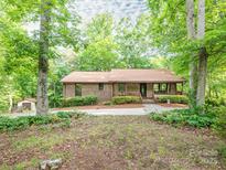 Charming brick home nestled among mature trees, boasting a covered front porch and lush landscaping at 9300 Surrey Rd, Mint Hill, NC 28227