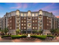 Elegant brick building with lush landscaping, fountain, and balconies against a colorful twilight sky at 4620 Piedmont Row Dr # 308, Charlotte, NC 28210