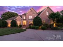 Striking brick home with manicured lawn and circular driveway, illuminated by warm lighting against a vibrant twilight sky at 1509 Churchill Downs Dr, Waxhaw, NC 28173