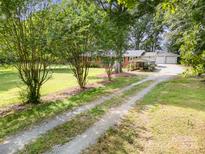Brick home with metal roof, detached garage, and gravel driveway lined with trees at 2320 Doster Rd, Monroe, NC 28112