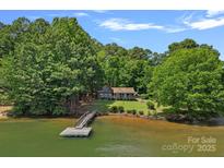 Waterfront home with dock surrounded by mature trees and landscaping on a sunny day at 2563 Brawley School Rd, Mooresville, NC 28117