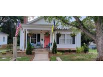 Charming cottage-style home with a welcoming porch, beautiful plants, and mature trees at 105 N Central Ave, Belmont, NC 28012