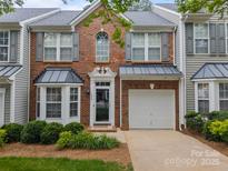 Charming brick townhouse featuring a one-car garage, black awnings, lush landscaping, and a welcoming entrance at 1647 Backcreek Ln, Gastonia, NC 28054