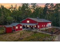 Beautiful red barn-style home with covered patio and professional landscaping at sunset at 574 Crescent Rd, Rockwell, NC 28138