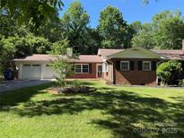 Charming brick home with an attached two-car garage, a well-manicured lawn, and lush trees surrounding the property at 121 33Rd Ne Ave, Hickory, NC 28601