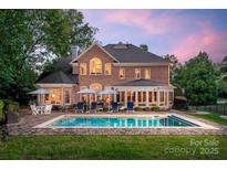 Stunning backyard oasis with a sparkling pool, patio, and ample seating at dusk at 15216 Ballantyne Country Club Dr, Charlotte, NC 28277
