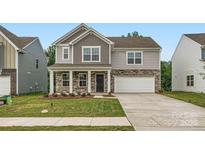 Charming two-story home with stone accents, a covered porch, a two-car garage, and a well-manicured lawn at 1545 Cottage Creek Dr, Bessemer City, NC 28016