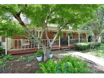 Inviting brick home featuring a charming front porch, mature tree, and lush landscaping at 109 Larch Rd, Salisbury, NC 28147
