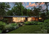 Twilight view of a landscaped home with illuminated interior, highlighting large windows and greenery at 2600 Cloister Dr, Charlotte, NC 28211