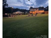 Evening shot of a spacious backyard with a pool, fire pit area, and a well-lit home, perfect for relaxation at 205 Wingate Dr, Stanley, NC 28164