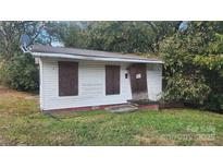 Exterior shot of a small, weathered home with boarded up windows and overgrown foliage at 210 Mahan Sw St, Concord, NC 28025