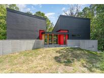 Modern black home featuring a red entryway, concrete accents, and lush green surroundings at 386 Squirrel Ln, Lake Wylie, SC 29710