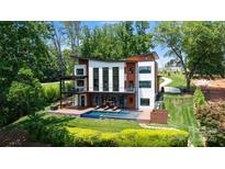 Modern two-story home with a pool and outdoor lounge area nestled in a lush, green landscape at 5930 Midsomer Rd, Charlotte, NC 28214