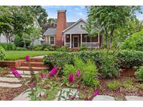 Charming brick home featuring a cozy front porch, lush landscaping, and a brick chimney at 1729 Kensington Dr, Charlotte, NC 28205