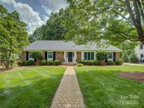 Charming brick home featuring a manicured lawn, mature landscaping, and welcoming walkway to the front door at 6116 Springhouse Ln, Charlotte, NC 28211