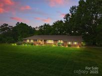 Charming brick home with a large lawn and professional landscaping, illuminated by soft lighting at dusk at 1081 Long Dr, Newton, NC 28658