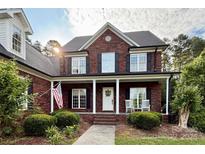 Beautiful two-story brick home with a well-manicured lawn, American flag, and a charming front porch with rocking chairs at 4230 Berry Hill Ct, Concord, NC 28025