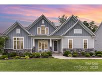 Charming home featuring stone accents, a well-manicured lawn, and a welcoming front porch with rocking chairs at 8709 Raven Top Dr, Mint Hill, NC 28227