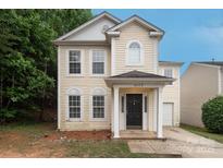 Two-story home with light yellow siding, black front door, and well-maintained front lawn and trimmed shrubs at 8432 Spirea Ct, Charlotte, NC 28215