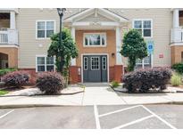 Apartment building entrance featuring a gray door, brick accents, and landscaped shrubs near parking at 11863 Ridgeway Park Dr, Charlotte, NC 28277