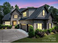 Charming gray brick home featuring a three-car garage, manicured lawn, and lush landscaping at 4143 Willow Haven Dr, Denver, NC 28037