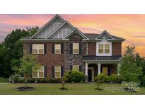 Elegant brick home featuring a stone facade, complemented by manicured landscaping and a welcoming front porch at 9032 Cornflower Dr, Harrisburg, NC 28075